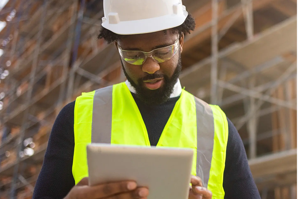 Une personne portant un gilet haute visibilité et un casque de chantier et utilisant une tablette.